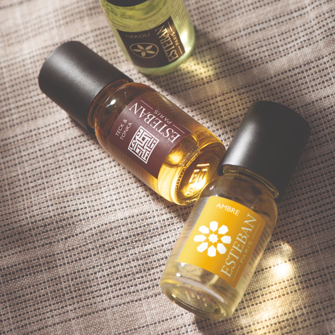 Huiles parfumées Esteban Paris Ambre, Néroli et Teck & Tonka, flacons concentrés de parfum présentés sur un tissu texturé dans une ambiance chaleureuse et raffinée