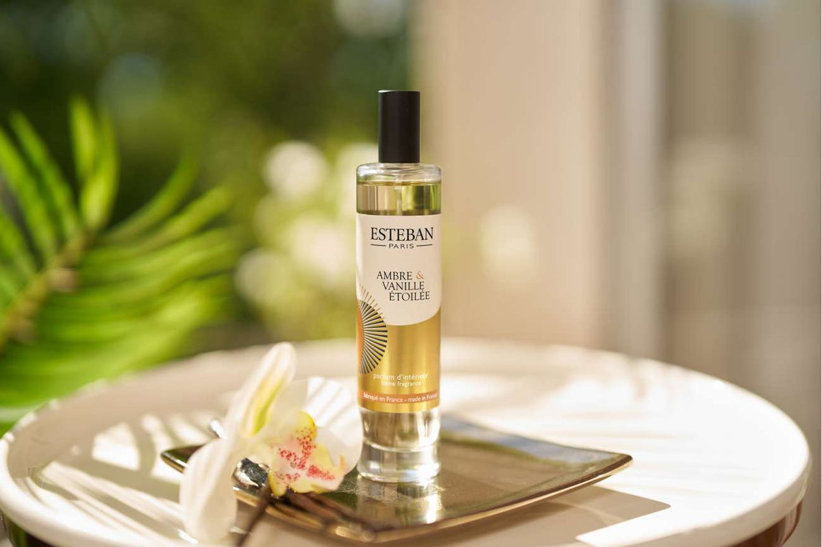 Parfum d’intérieur Esteban Paris Ambre & Vanille Étoilée en spray, flacon vaporisateur en verre transparent présenté sur un plateau doré avec une fleur blanche